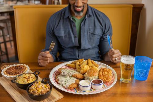 A man smiles at a large platter of fried food, with sides and drinks on the table, ready to enjoy his meal.