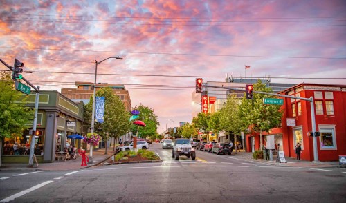 A vibrant street scene at sunset, featuring shops, traffic lights, and colorful clouds in the sky.