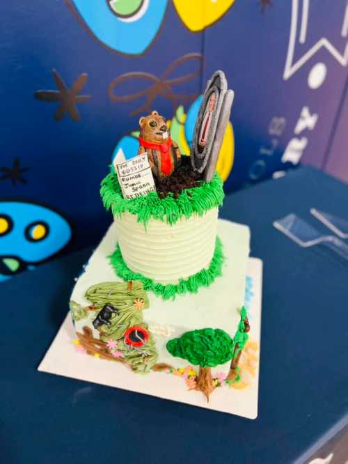 A whimsical cake featuring a bear figurine, a sign, and colorful decorations, set against a playful background.