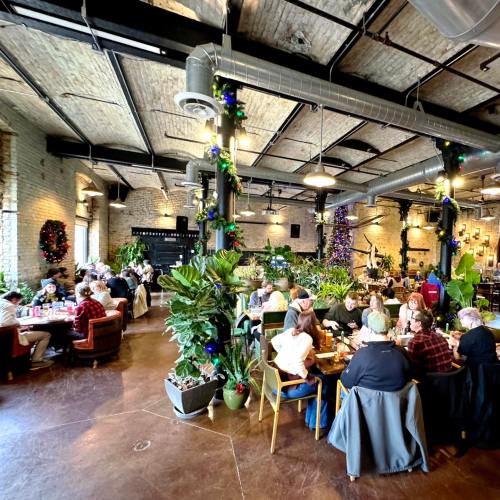 A bustling restaurant interior with diners at tables, decorated with plants and festive holiday decor.