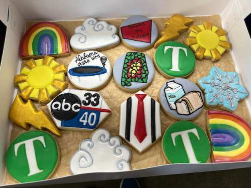 A box of colorful decorated cookies featuring rainbows, clouds, suns, and various themed designs.