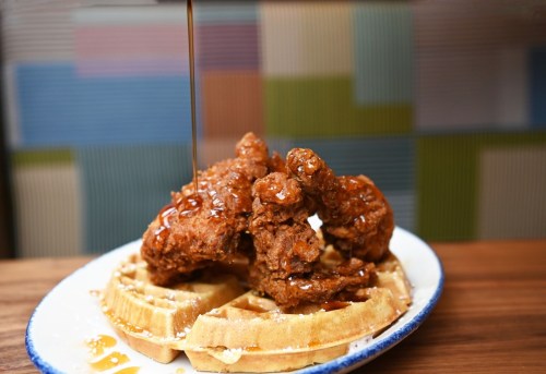 A plate of waffles topped with crispy fried chicken, drizzled with syrup.