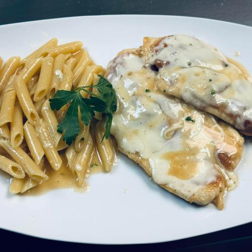 A plate of pasta and two chicken fillets topped with melted cheese and a drizzle of sauce, garnished with parsley.
