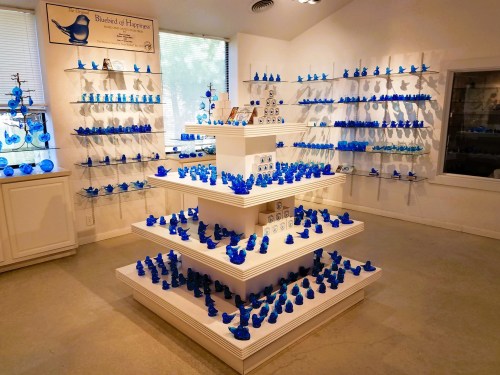 A display of various blue bird figurines arranged on white shelves in a bright, well-lit room.