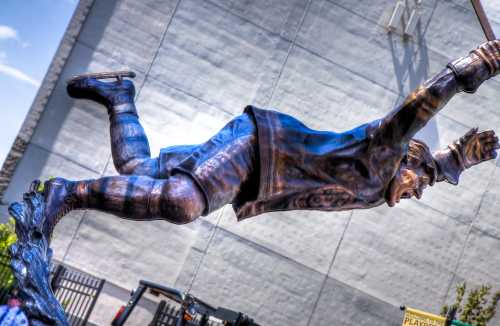 A bronze statue of a man in mid-air, seemingly skating, with a dynamic pose against a gray background.