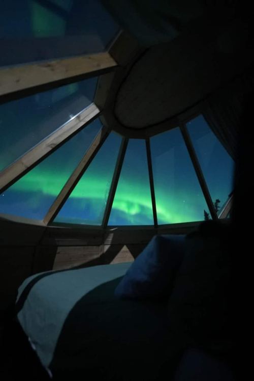 A cozy room with a glass ceiling showcasing the vibrant northern lights in the night sky.