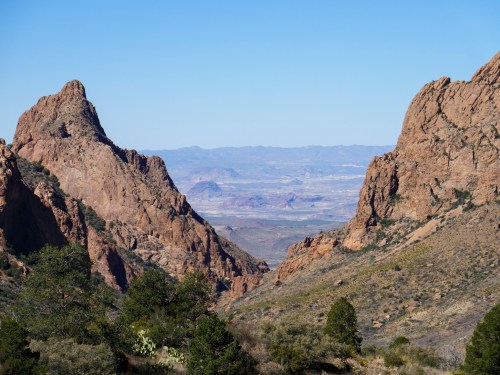 A scenic view of rugged mountains and valleys under a clear blue sky, showcasing natural rock formations and greenery.