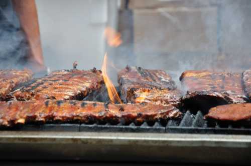 Grilled ribs sizzling on a barbecue, with flames and smoke rising from the hot grill.