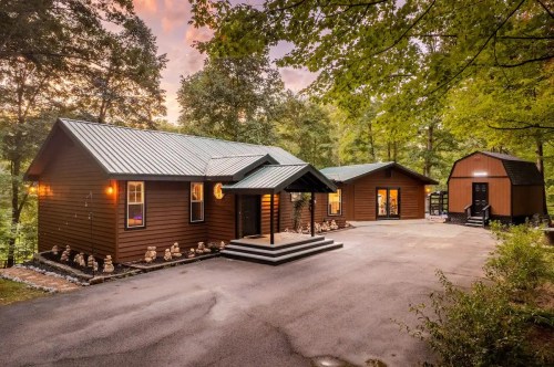 A modern brown cabin surrounded by trees, featuring a welcoming entrance and a driveway at sunset.