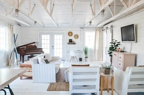Bright, airy living room with white walls, a piano, plants, and cozy furniture, featuring large windows and wooden accents.