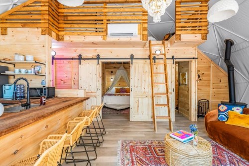 Cozy wooden interior of a modern cabin with a loft, featuring a kitchen bar, seating area, and warm decor.
