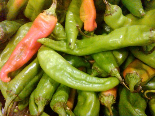 A close-up of various chili peppers, including green and red varieties, piled together.