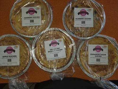 Five pies wrapped in plastic, labeled Juneberry, Blueberry, Strawberry Rhubarb, Apple, and Cinnamon/Sugar Kuchen.