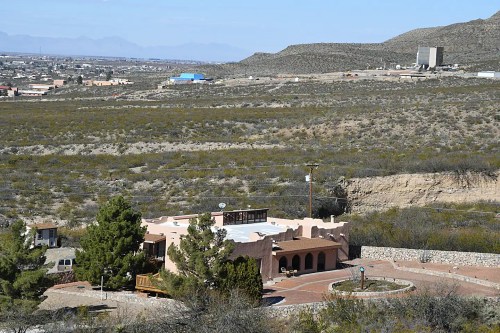 Aerial view of a southwestern-style building surrounded by desert landscape and mountains in the background.