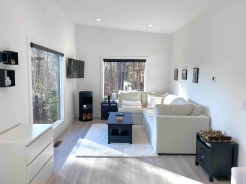 Bright, modern living room with a white sofa, black coffee table, and large windows overlooking a wooded area.