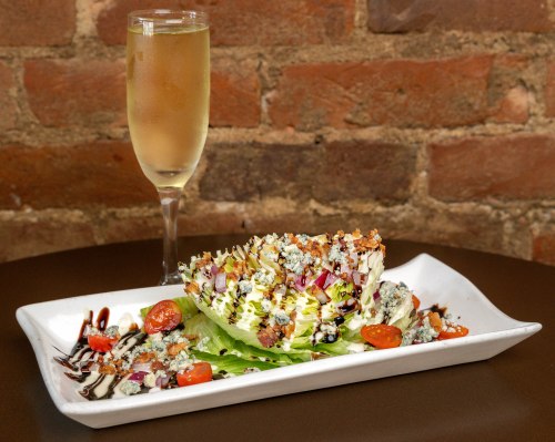 A wedge salad topped with blue cheese, cherry tomatoes, and nuts, served with a glass of sparkling wine.