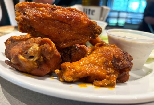 A plate of crispy, sauced chicken wings with a side of dipping sauce.