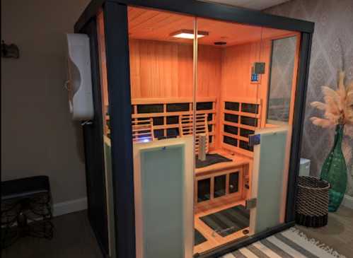 A wooden sauna with glass walls, featuring benches and soft lighting, set in a cozy indoor space.