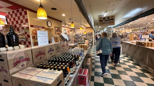 A bustling market aisle filled with boxes, bottles, and shoppers exploring various food products.