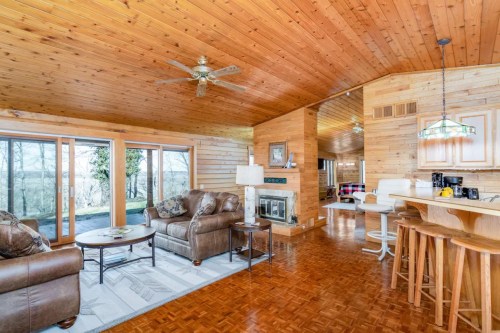 Cozy wooden living room with a fireplace, large windows, and a kitchen bar area, featuring comfortable seating.