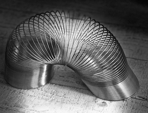 A metallic slinky toy positioned on a textured surface, creating a curved, spiral shape in black and white.