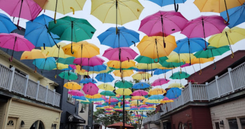 Colorful umbrellas in shades of pink, blue, and yellow hang overhead in a charming street scene.