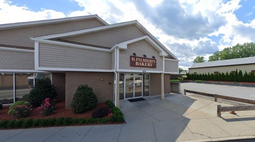 Exterior view of D. Palmieri's Bakery, featuring a sign, landscaped area, and a cloudy sky in the background.