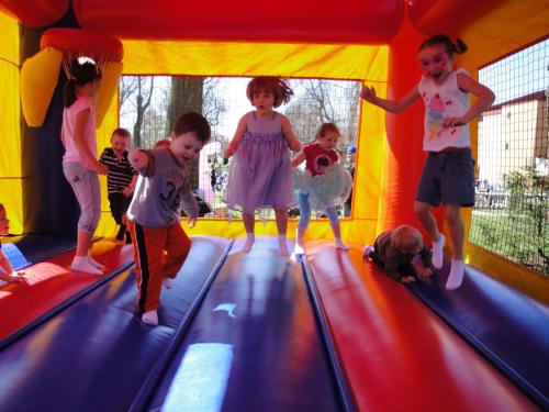 Children joyfully jumping in a colorful bounce house on a sunny day, with some wearing playful outfits and face paint.