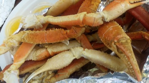 A close-up of cooked crab legs arranged on a plate, with dipping sauces in small containers nearby.