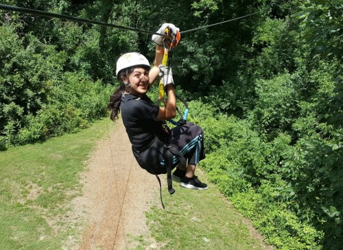 A person in a helmet zip-lining through a lush green forest, smiling as they glide along the cable.