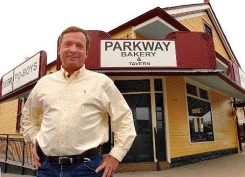 A man stands confidently in front of the Parkway Bakery & Tavern, a yellow building with a red awning.