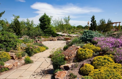 A scenic garden path lined with colorful flowers and greenery under a bright blue sky.