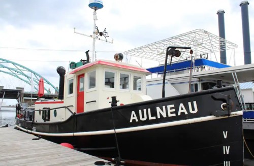 A black and white boat named "AULNEAU" docked at a pier, with a cloudy sky in the background.