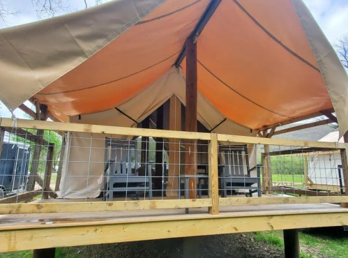 A glamping tent with a wooden deck and two chairs, surrounded by greenery.