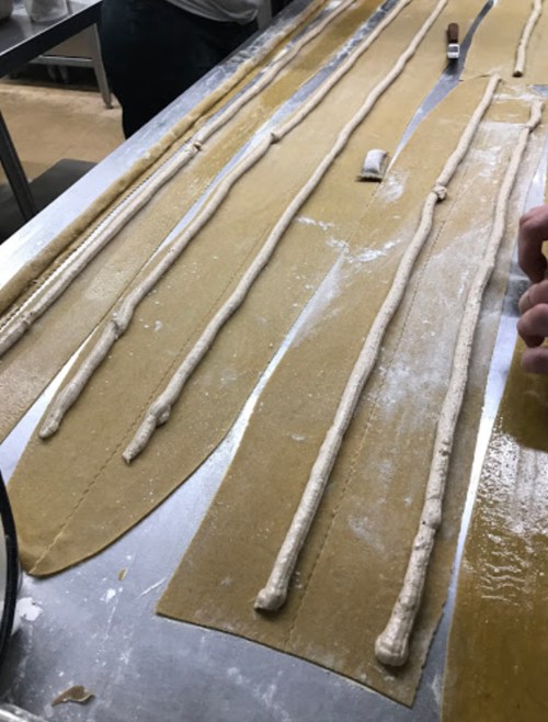 Fresh pasta dough laid out on a countertop, with lines of filling being piped onto the sheets.