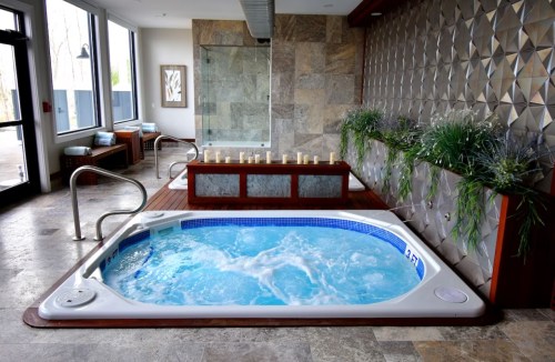 A modern spa area featuring a bubbling hot tub, stone walls, and greenery, creating a relaxing atmosphere.
