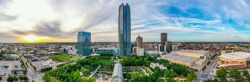 A panoramic view of a city skyline at sunset, featuring tall buildings and green spaces.