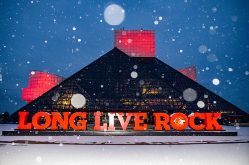 The Rock and Roll Hall of Fame illuminated at night, with "LONG LIVE ROCK" in bold orange against a snowy backdrop.