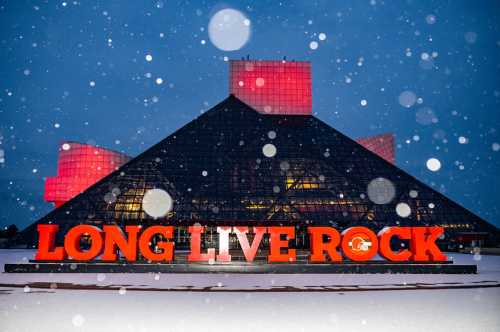 The Rock and Roll Hall of Fame illuminated at night, with "LONG LIVE ROCK" in bold orange against a snowy backdrop.