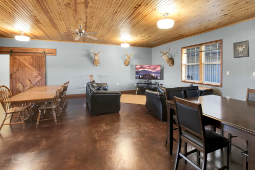 Cozy interior with wooden ceiling, dining area, leather sofas, and mounted deer heads on the wall.