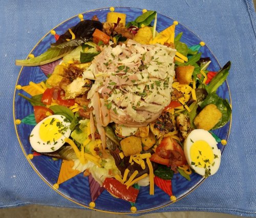 A colorful salad topped with sliced turkey, cheese, croutons, and halved boiled eggs on a decorative plate.