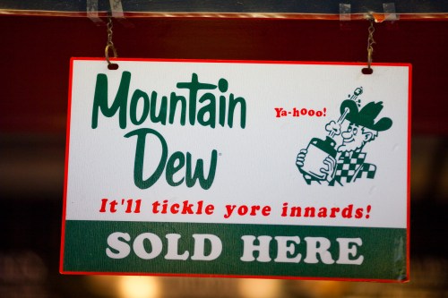 A sign advertising Mountain Dew with a playful slogan, featuring a cartoon cowboy holding a drink.