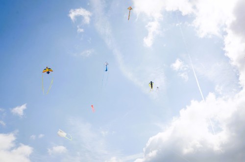 Colorful kites flying high in a blue sky with fluffy white clouds.