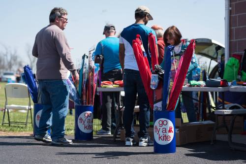 People browsing a kite festival booth with colorful kites and umbrellas on display under a clear blue sky.