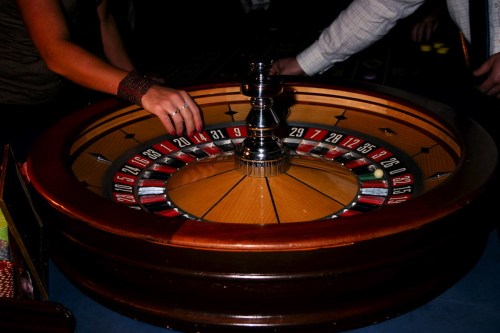 A close-up of a roulette table with a hand placing a bet on the spinning wheel.