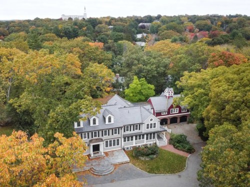 Aerial view of a large house surrounded by colorful autumn trees and a nearby red barn-style building.
