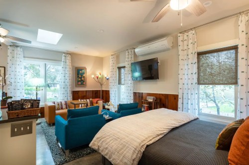 Cozy room featuring a bed, blue sofas, a TV, and large windows with natural light and decorative curtains.