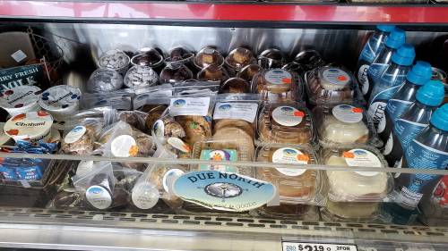 A display case filled with various desserts and bottled water, labeled "DUE NORTH." Prices are visible on some items.