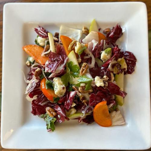 A colorful salad with radicchio, apples, carrots, nuts, and herbs, served in a white square dish.