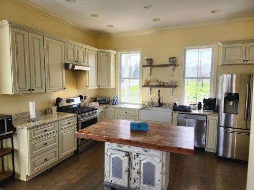Bright kitchen with cream cabinets, granite countertops, a wooden island, and large windows overlooking greenery.